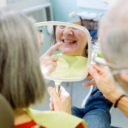 Patientin betrachtet Zähne im Spiegel